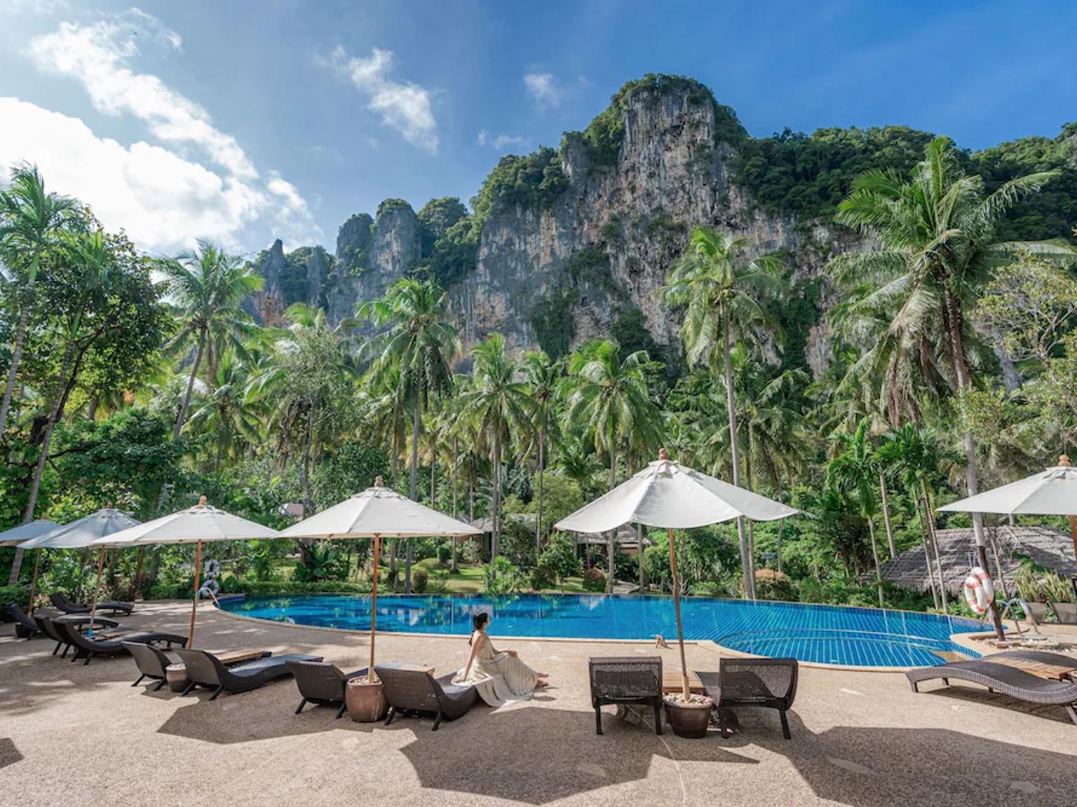 en kvinne sitter på en stol ved siden av et svømmebasseng med paraplyer