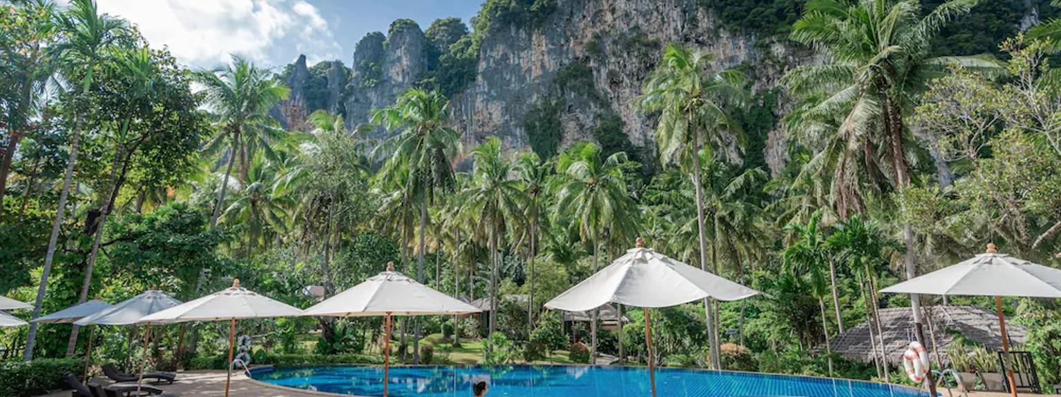 en kvinne sitter på en stol ved siden av et svømmebasseng med paraplyer