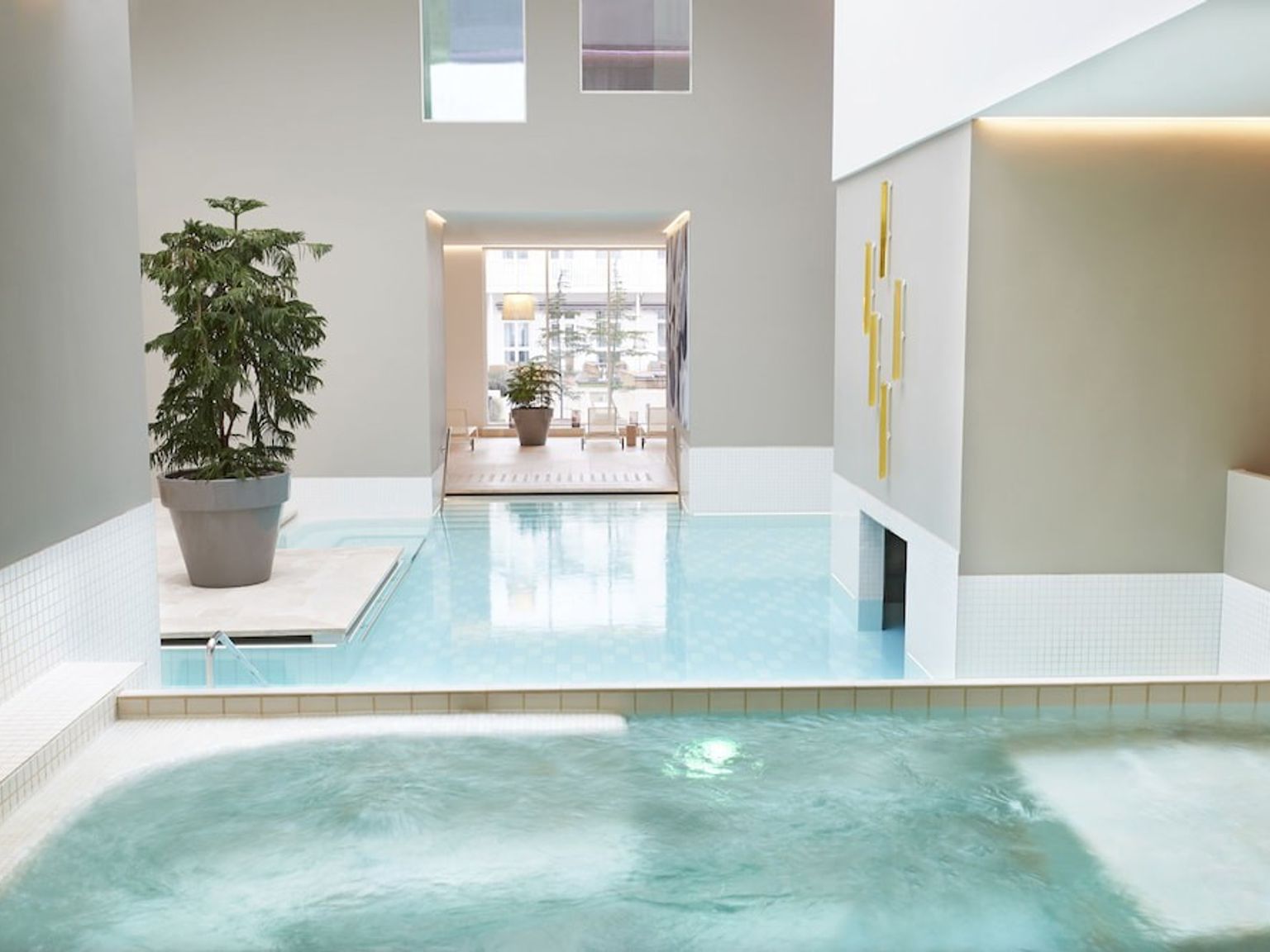 Et moderne indendørs spaområde med lyseblå pools, en stor potteplante og gyldent vægdekoration.