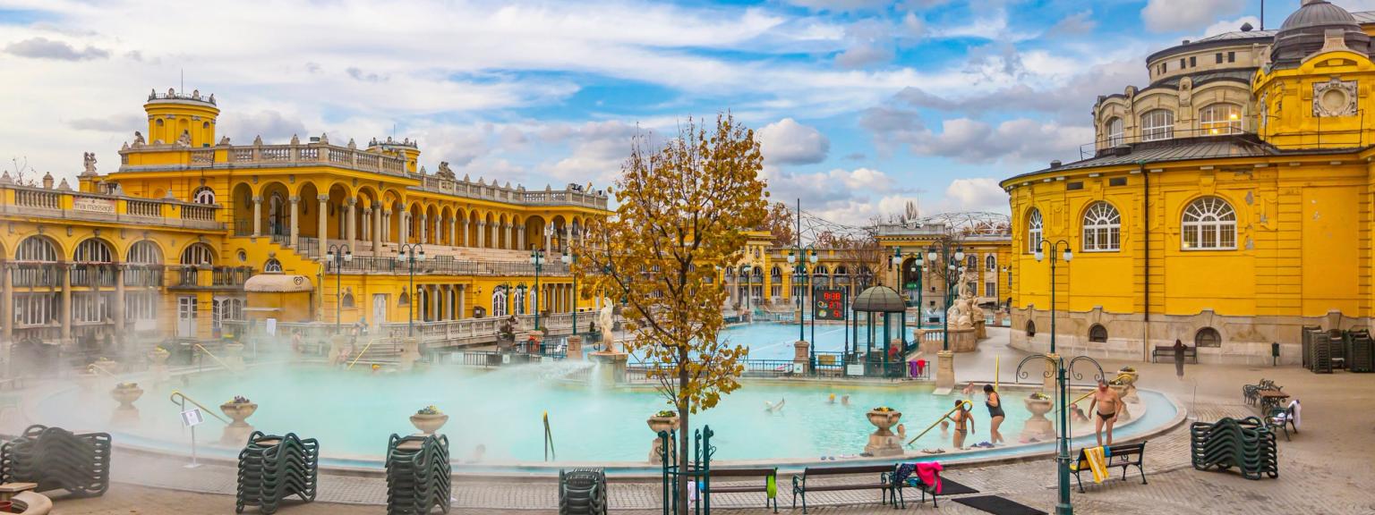 en gruppe mennesker svømmer i et stort basseng foran en bygning i Budapest.