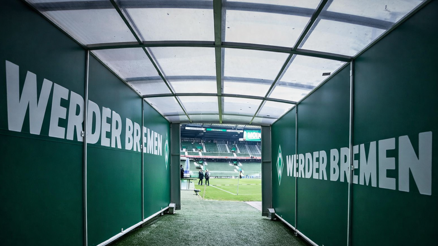 A green tunnel with "WERDER BREMEN" branding leads out to a football stadium pitch.