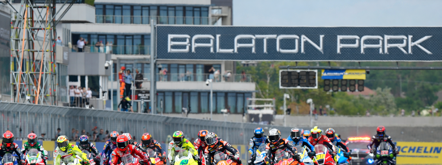 Motorracers leunen in een bocht op een circuit, met daarboven spandoeken met de tekst "Michelin" en "Balaton Park".