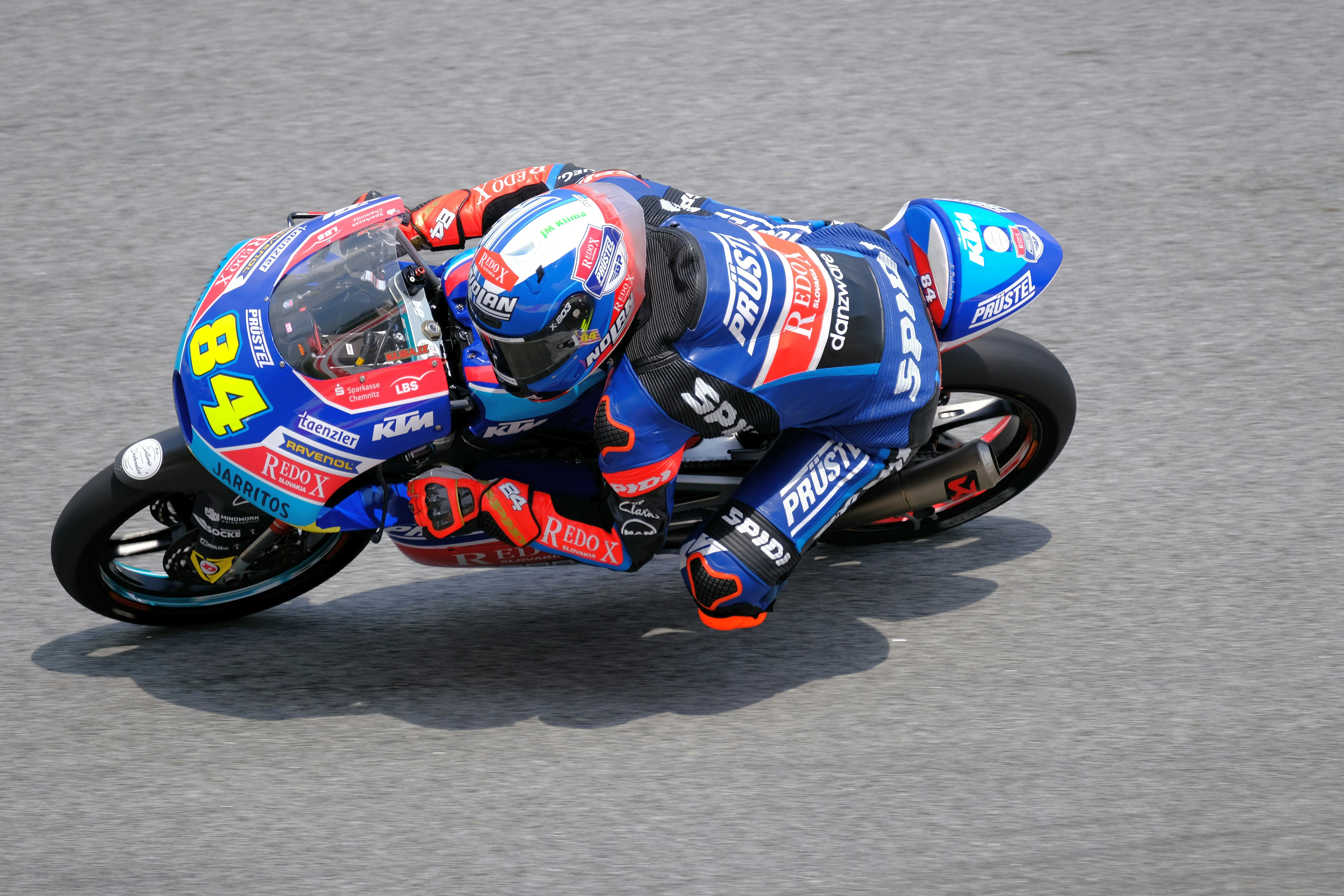Motorcycle racer number 84 in a blue suit leans sharply into a turn on a blue and white bike.