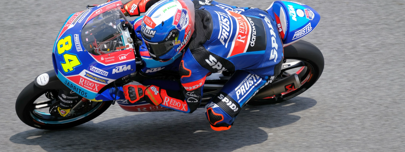 Motorcycle racer number 84 in a blue suit leans sharply into a turn on a blue and white bike.