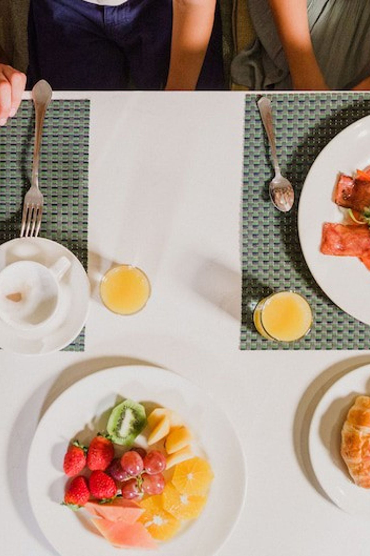 Overhead view of a breakfast table with plates of eggs, bacon, fruit, pastries, waffles, and juice, with people's hands visible. Aparthotel Club del Sol Resort & SPA