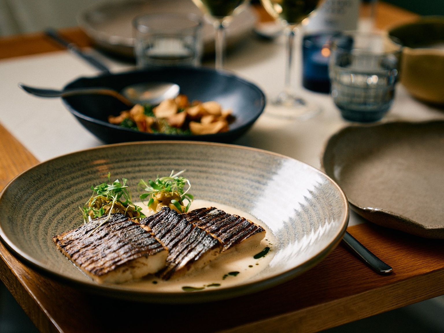 Paistetut kalafileet kermakastikkeella ja mikrovihreillä teksturoidulla lautasella ravintolassa.