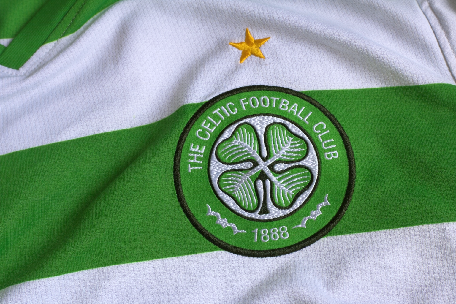 Escudo bordado del Celtic FC y estrella dorada en una camiseta a rayas verdes y blancas.