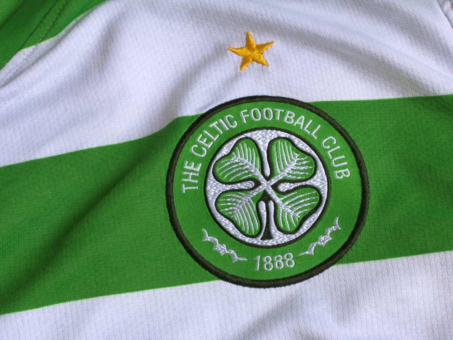 Broderad Celtic FC-emblem och guldstjärna på en grön och vit randig tröja.
