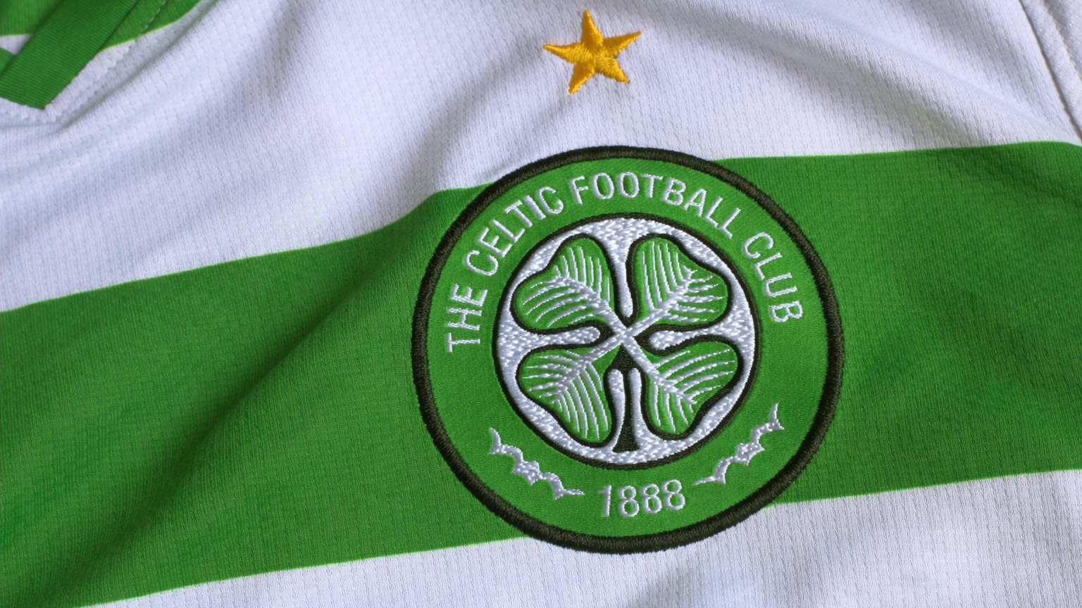 Escudo bordado del Celtic FC y estrella dorada en una camiseta a rayas verdes y blancas.