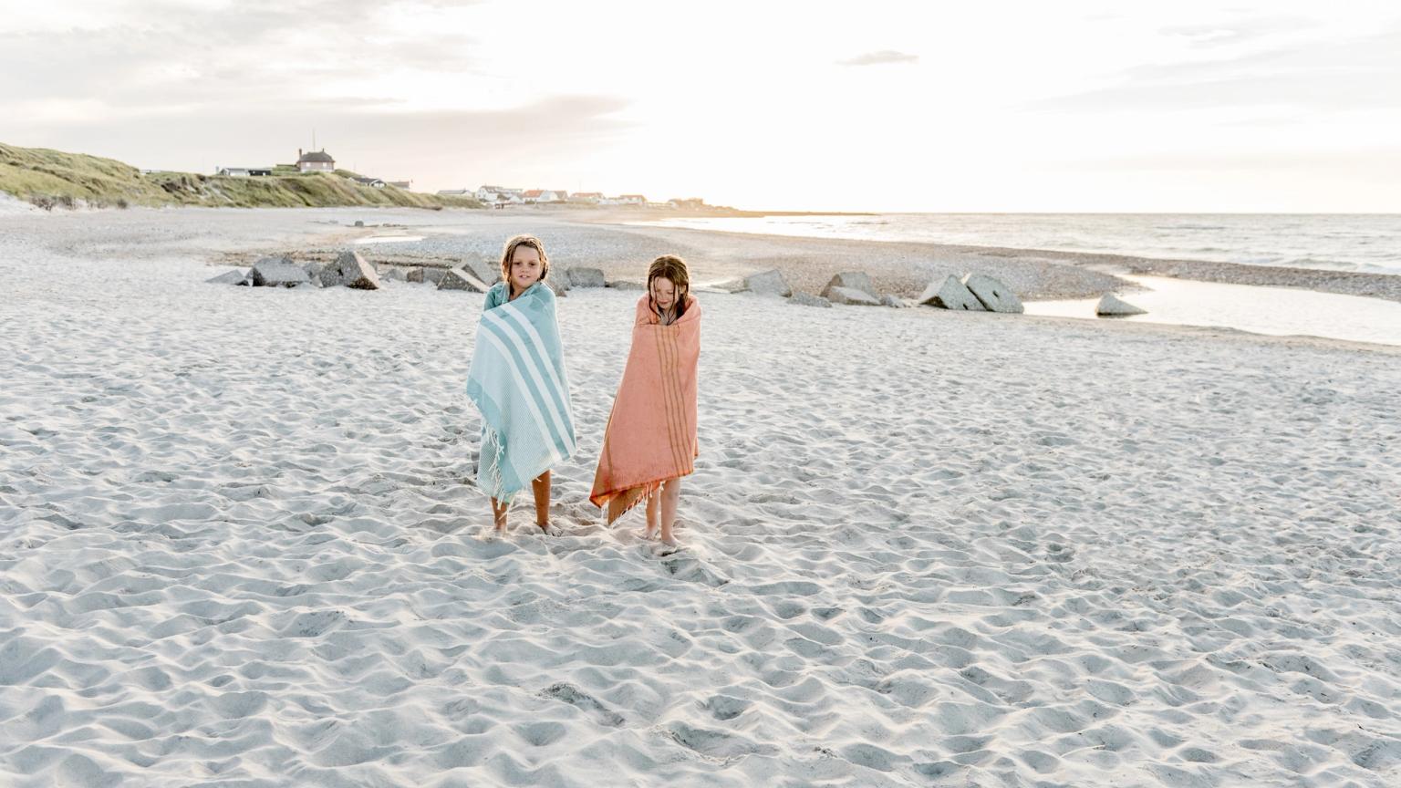 två tjejer inslagna i handdukar går på stranden
