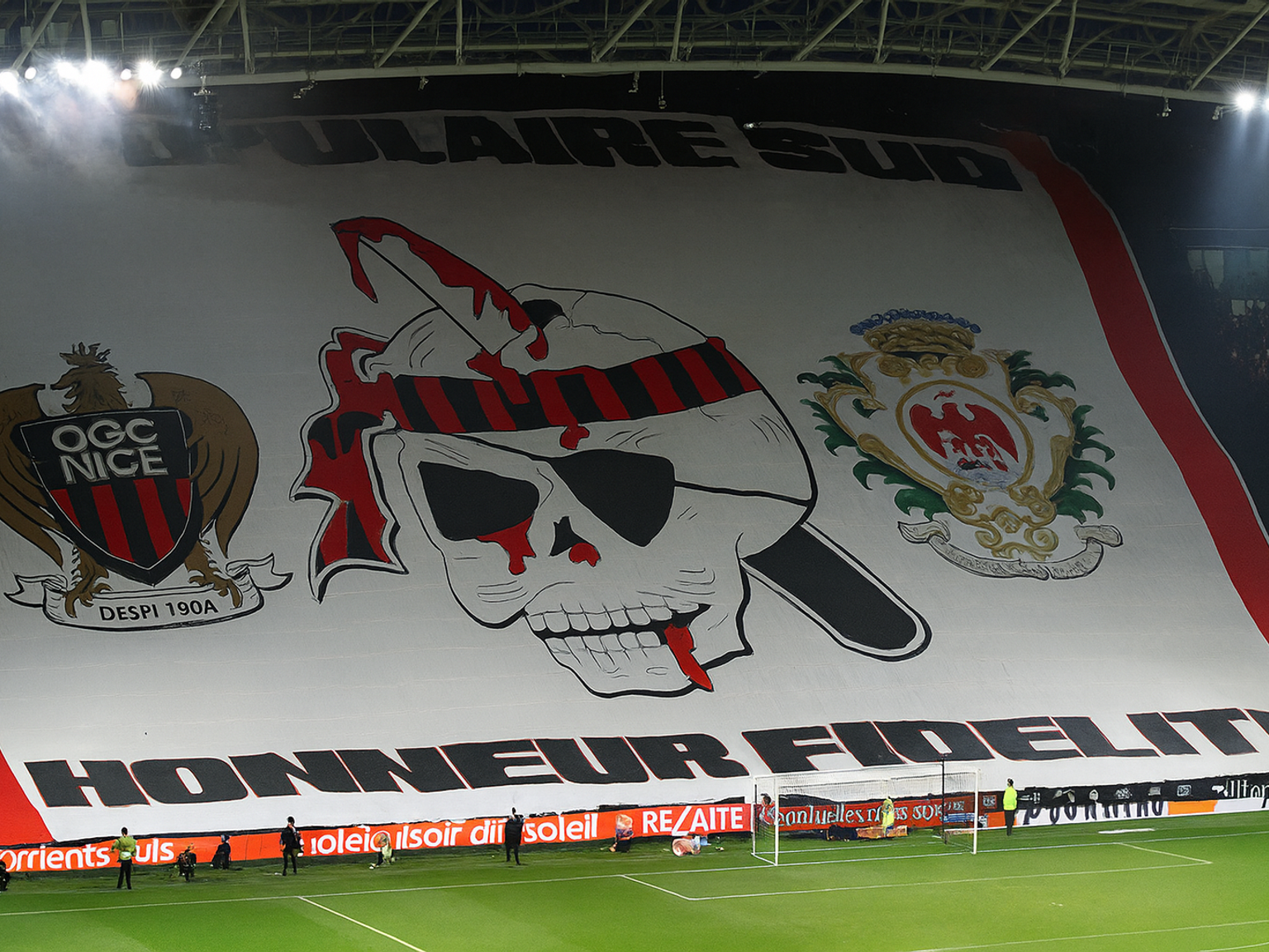 Grande tifo de estádio com o brasão do OGC Nice, um crânio sangrento com uma faca, o emblema da cidade de Nice e o texto "POPULAIRE SUD" e "HONNEUR FIDELITE."