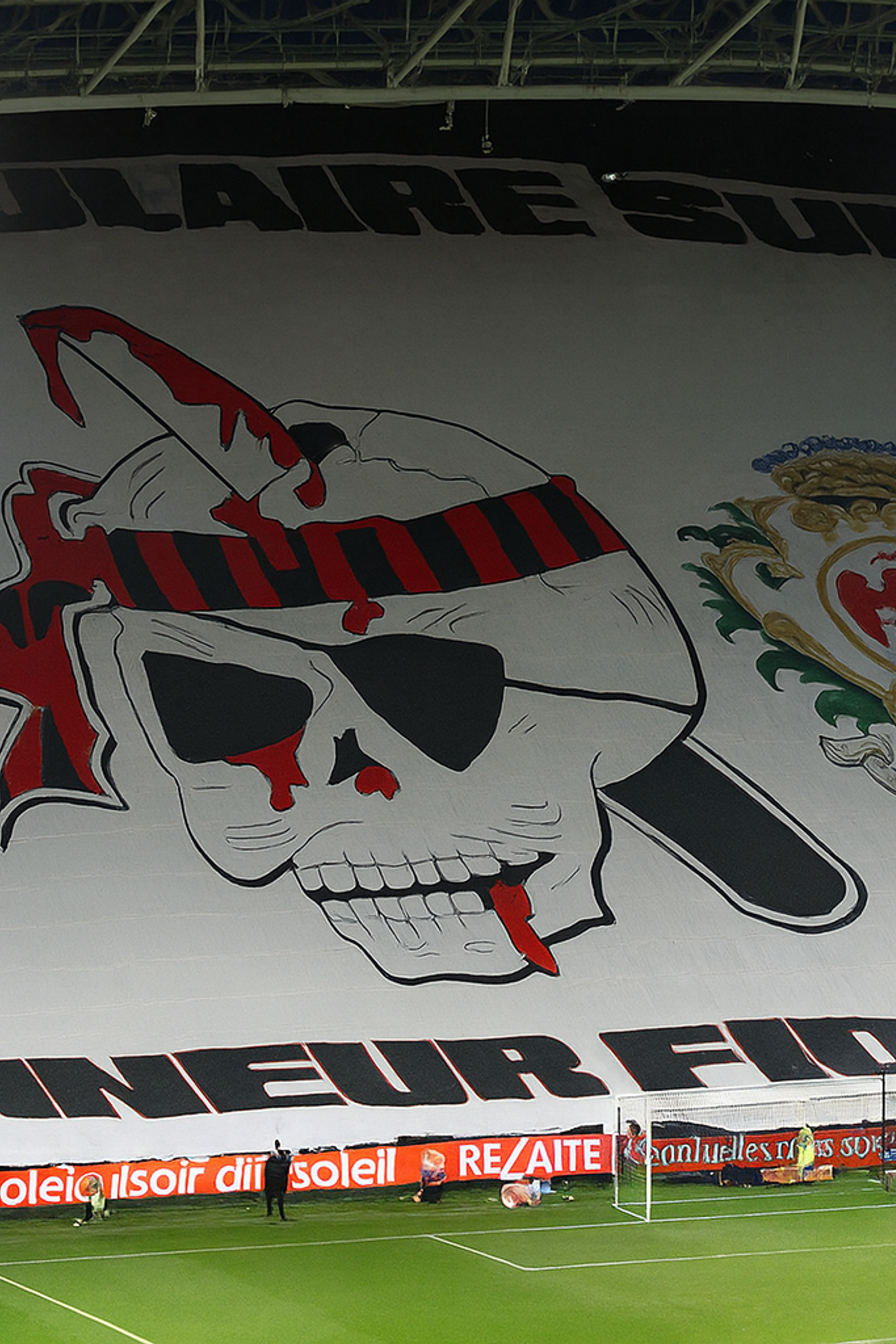 Grande tifo de estádio com o brasão do OGC Nice, um crânio sangrento com uma faca, o emblema da cidade de Nice e o texto "POPULAIRE SUD" e "HONNEUR FIDELITE."