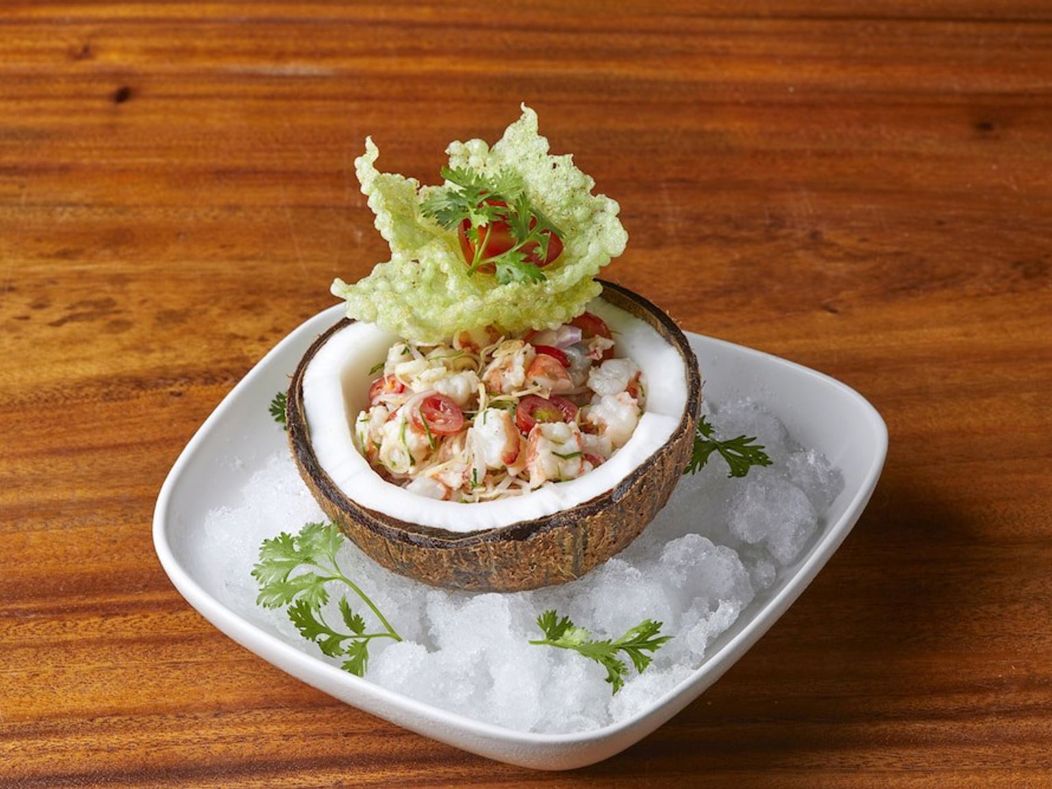 ein Salat in einer Kokosnussschale auf Eis auf einem Holztisch