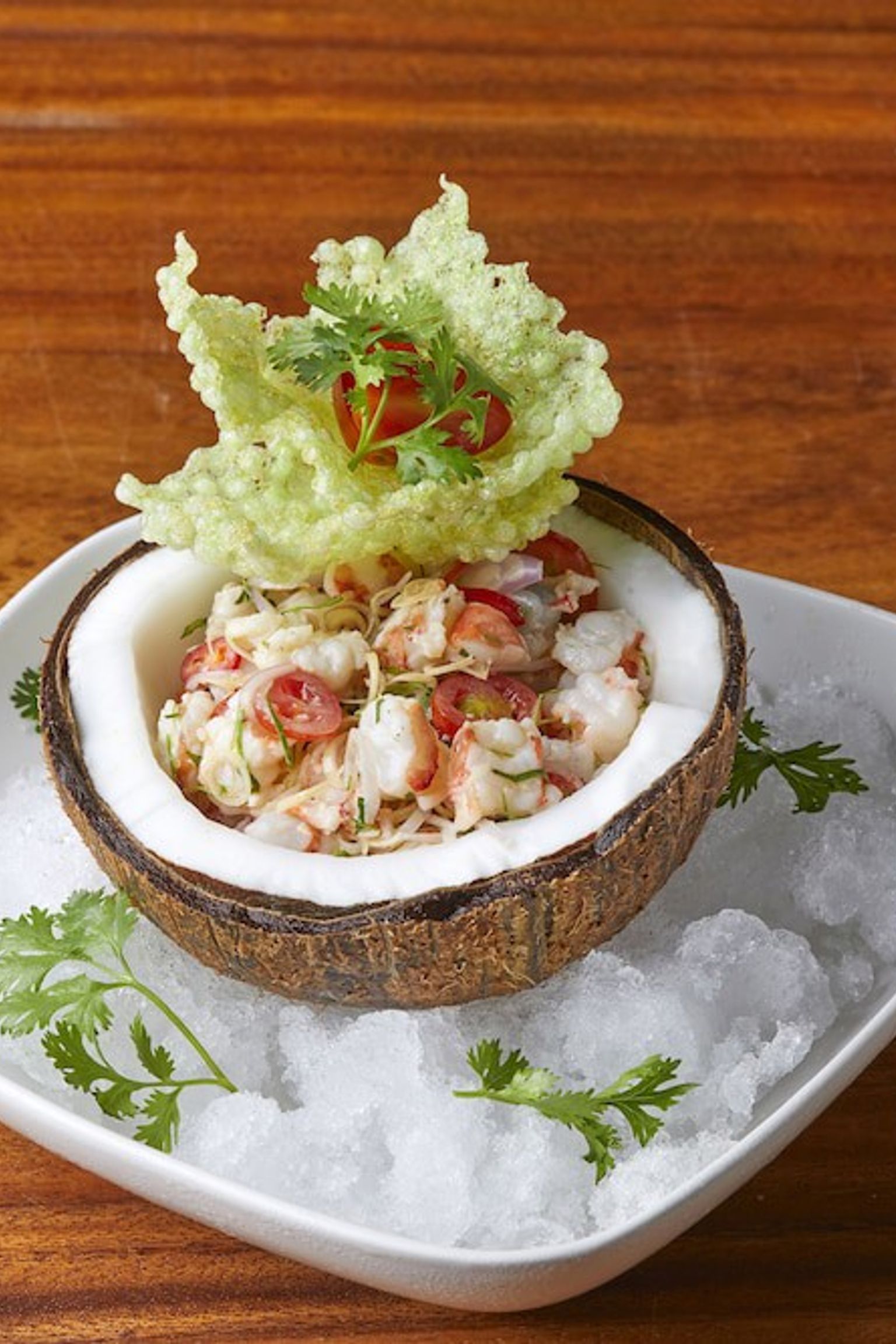 ein Salat in einer Kokosnussschale auf Eis auf einem Holztisch