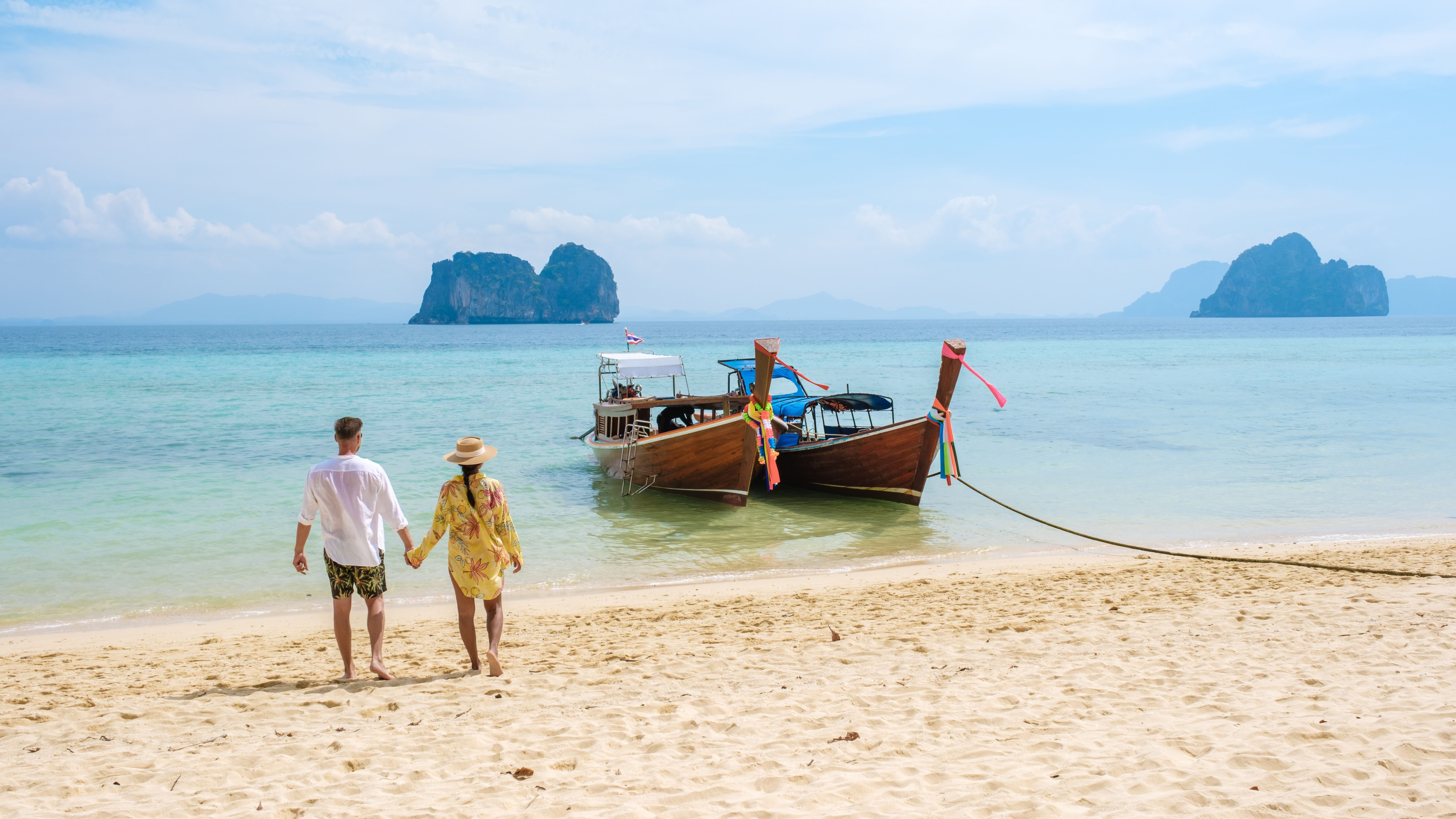 en mann og en kvinne går på en strand ved siden av båter.