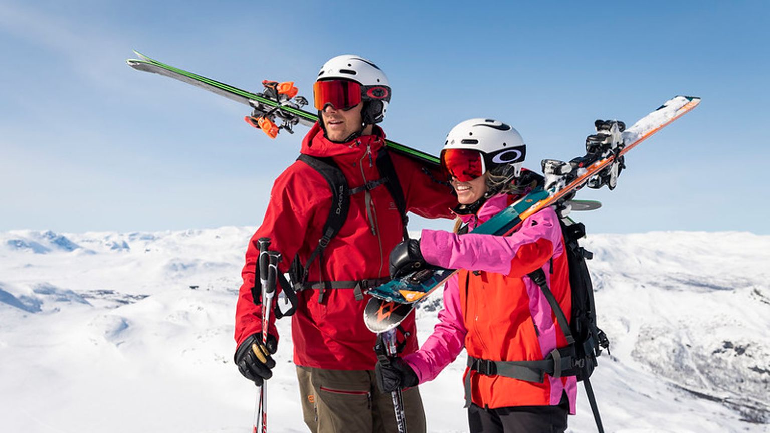 en mann og en kvinne står på toppen av et snødekket fjell og holder ski