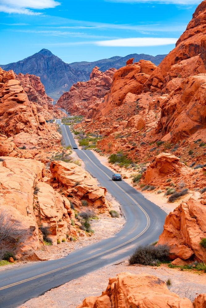 Snoet vej gennem orange klippeformationer, fjerne bjerge og blå himmel. Valley of Fire