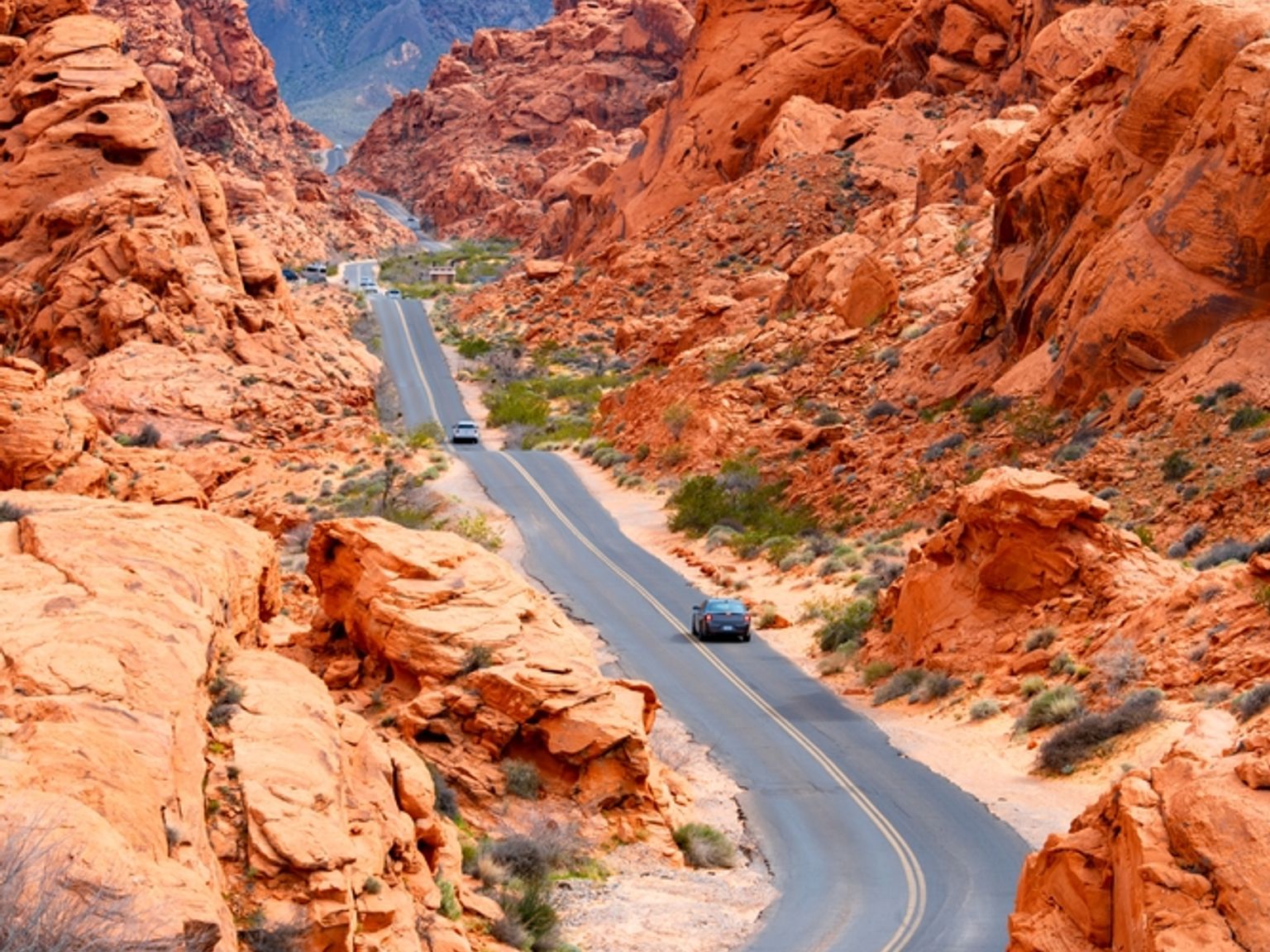 Svingete vei gjennom oransje fjellformasjoner, fjerne fjell og blå himmel. Valley of Fire
