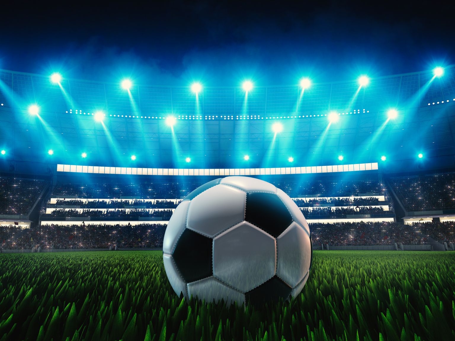 en fotball sitter på gresset foran et stadion om natten