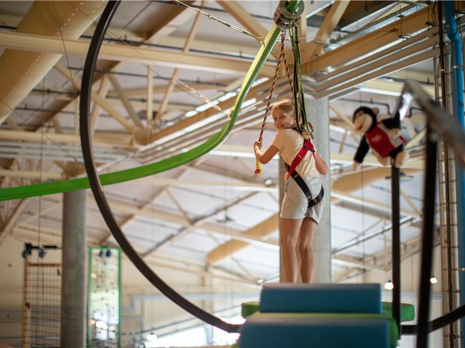 Ung pige i sele smiler på en indendørs adventurebane. Lalandia Resort Søndervig