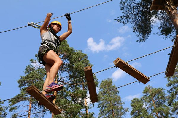 A woman wearing a helmet and harness walks across a high ropes course obstacle.