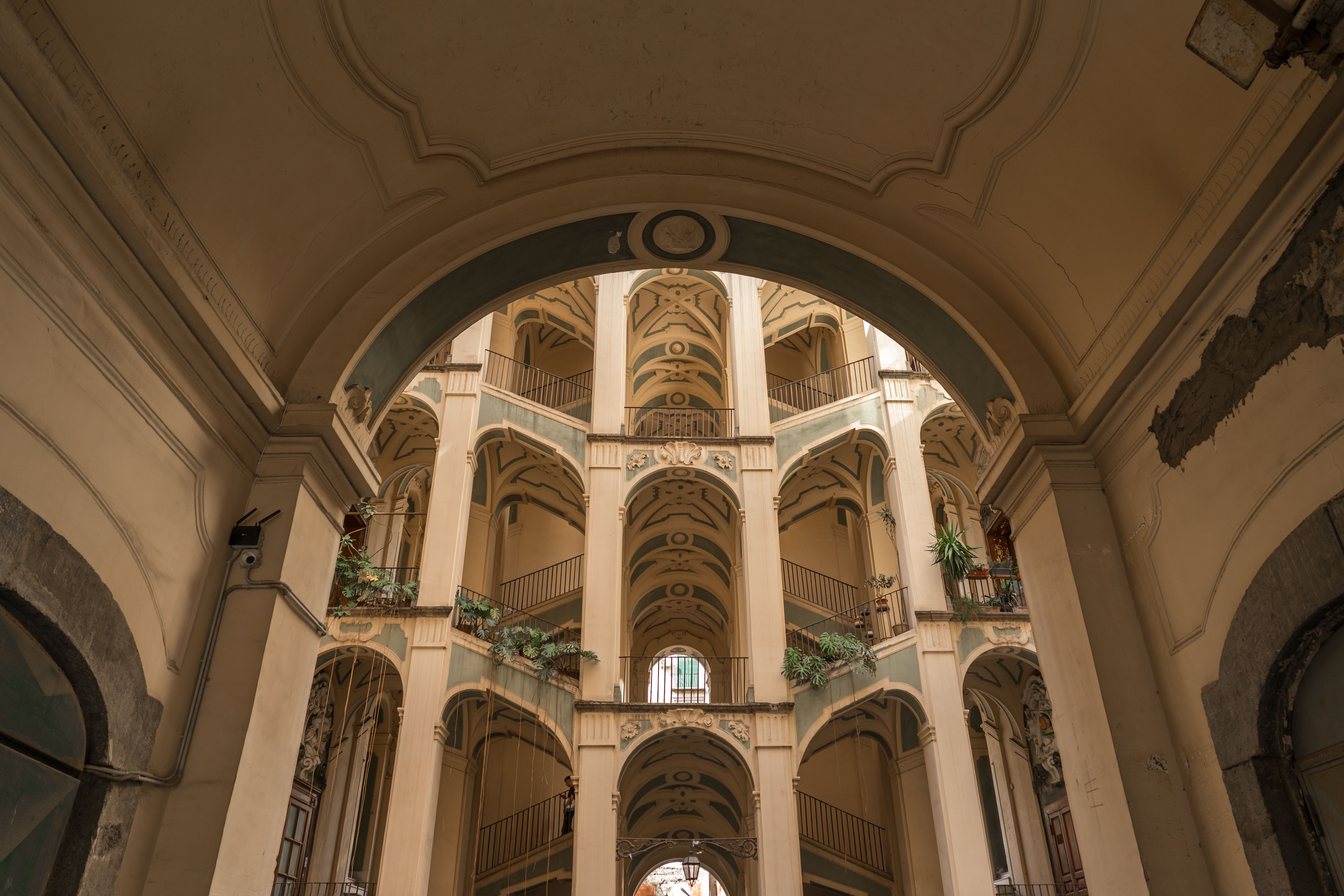 Intérieur orné sur plusieurs étages avec des balcons voûtés empilés et un grand escalier sinueux, peint en crème et bleu sarcelle.