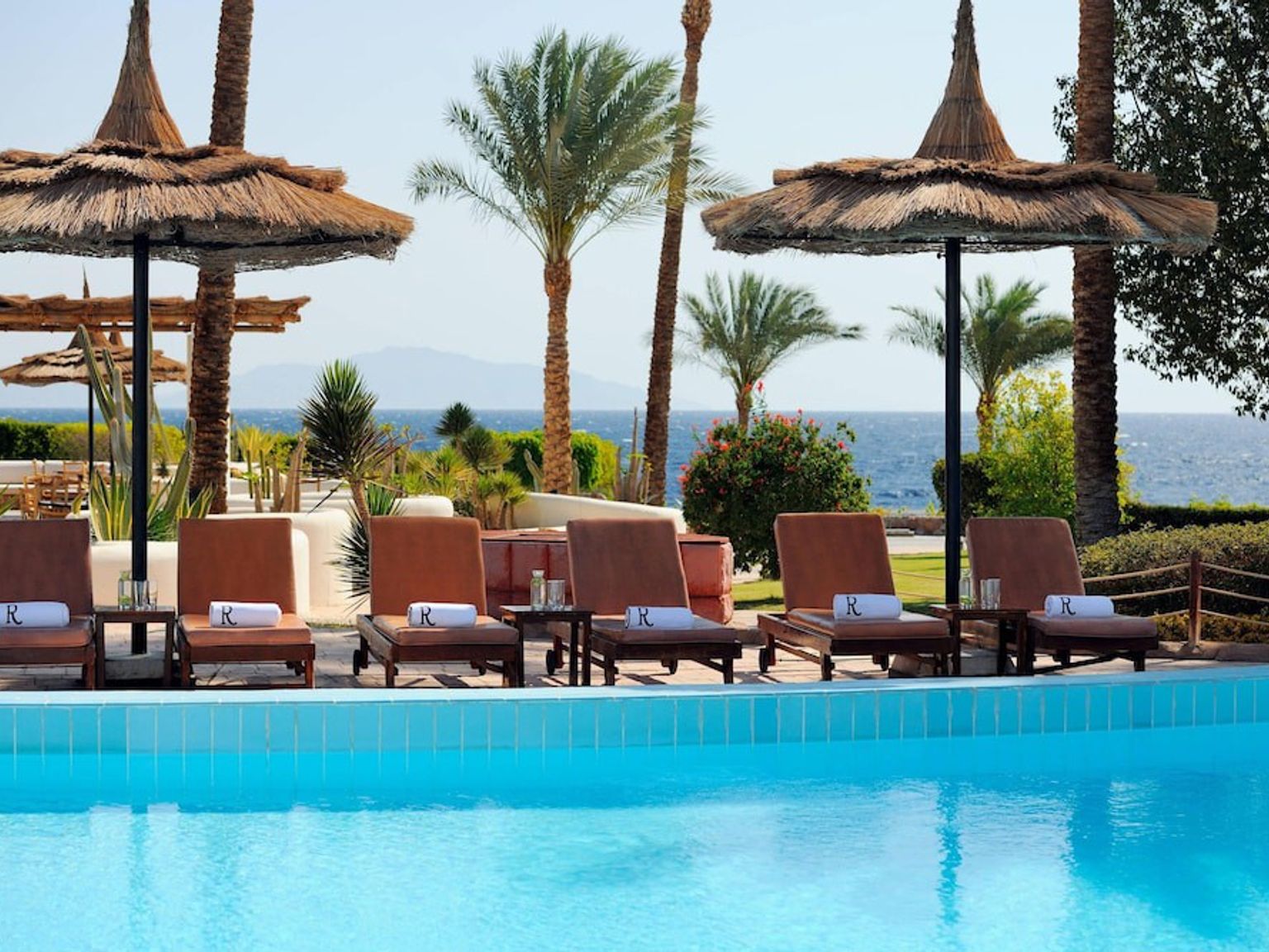 ein Schwimmbad umgeben von Stühlen und Sonnenschirmen mit Blick auf das Meer
