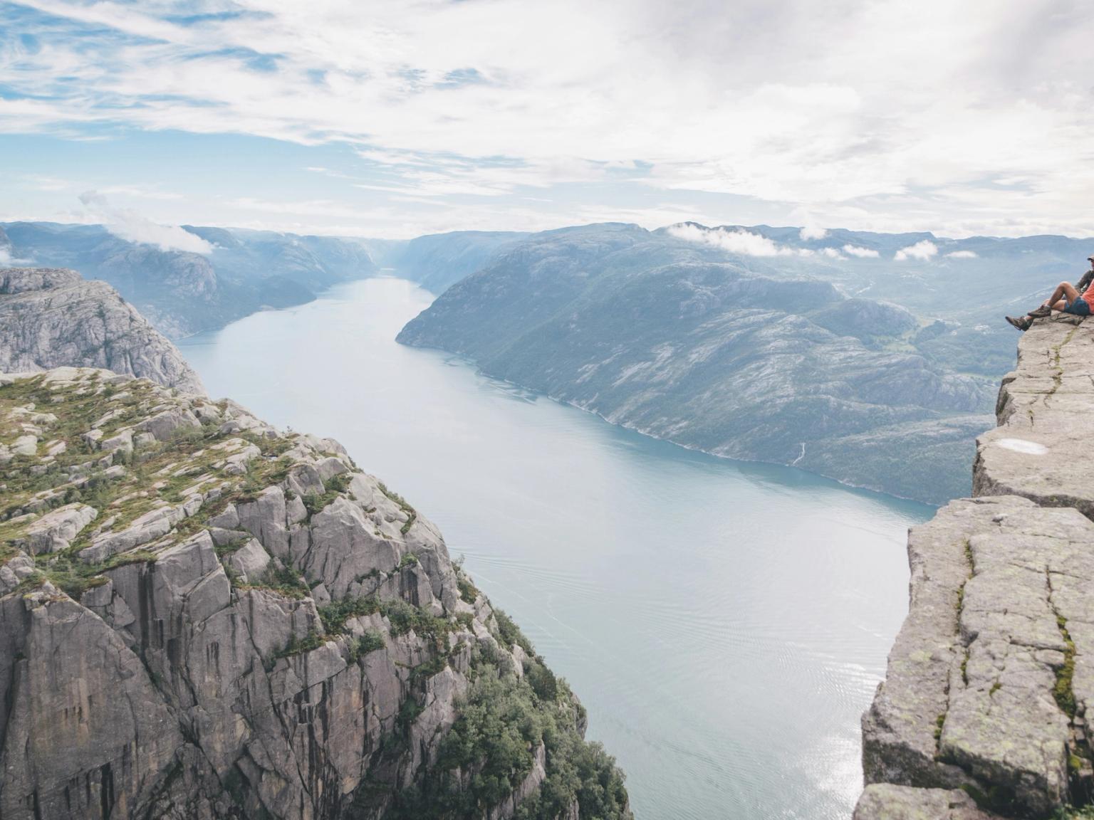 ein Mann sitzt am Rand einer Klippe und blickt auf einen See