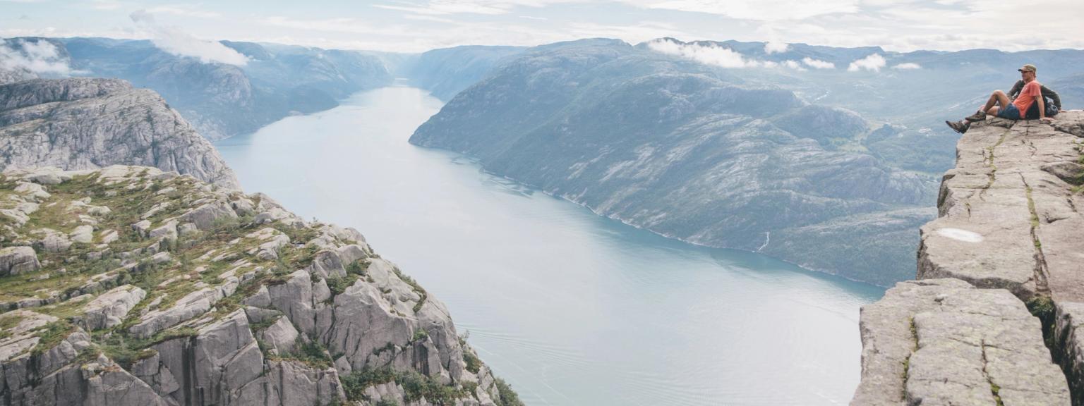 en man sitter på kanten av en klippa med utsikt över en sjö
