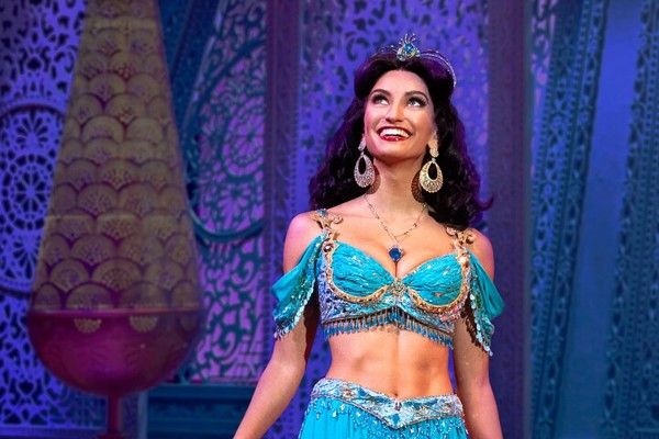 Une femme portant un costume turquoise de la princesse Jasmine sourit et regarde vers la scène.