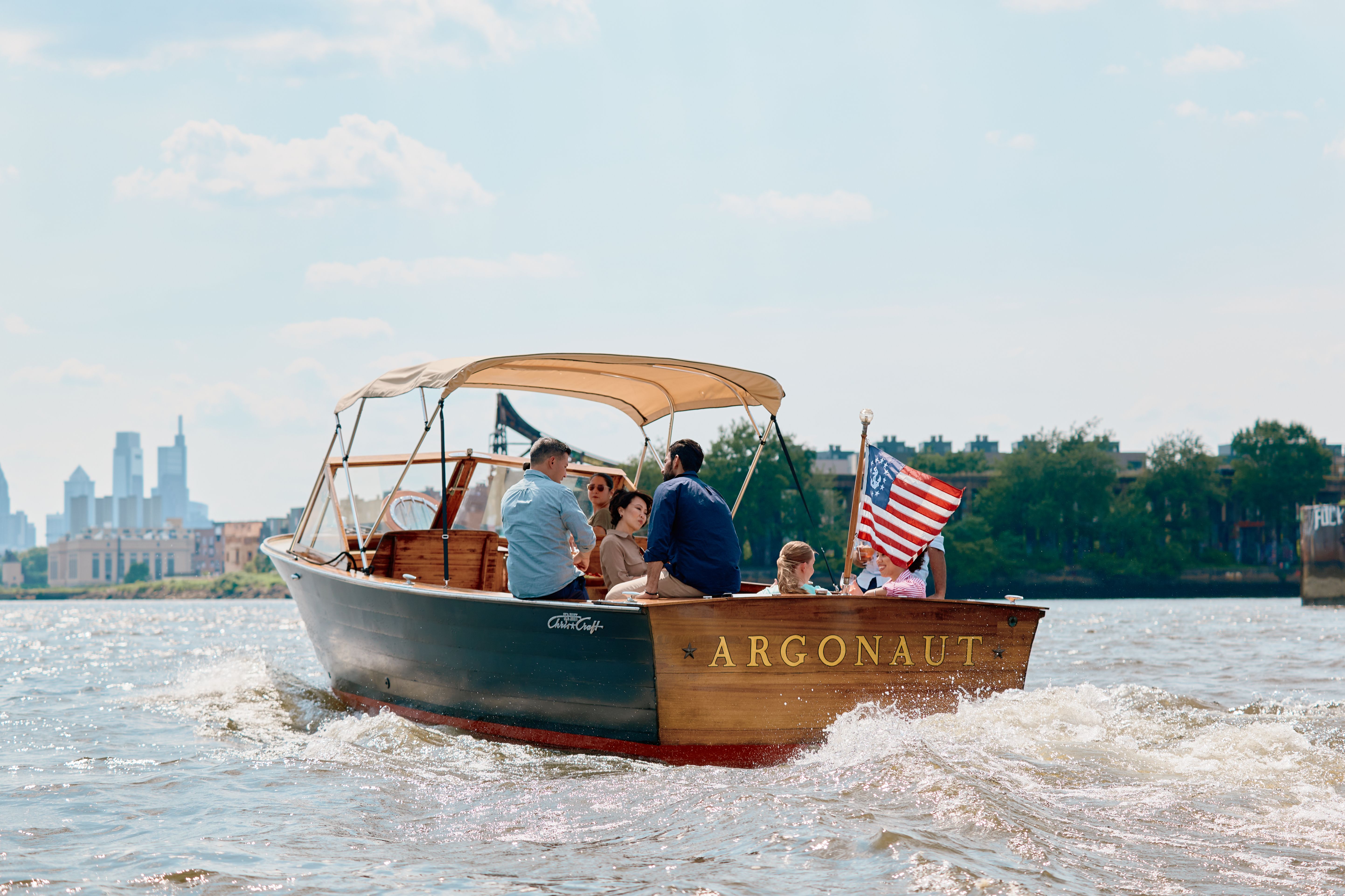 En båd ved navn "ARGONAUT" transporterer passagerer på en flod med en bysilhuet i baggrunden. Philadelphia