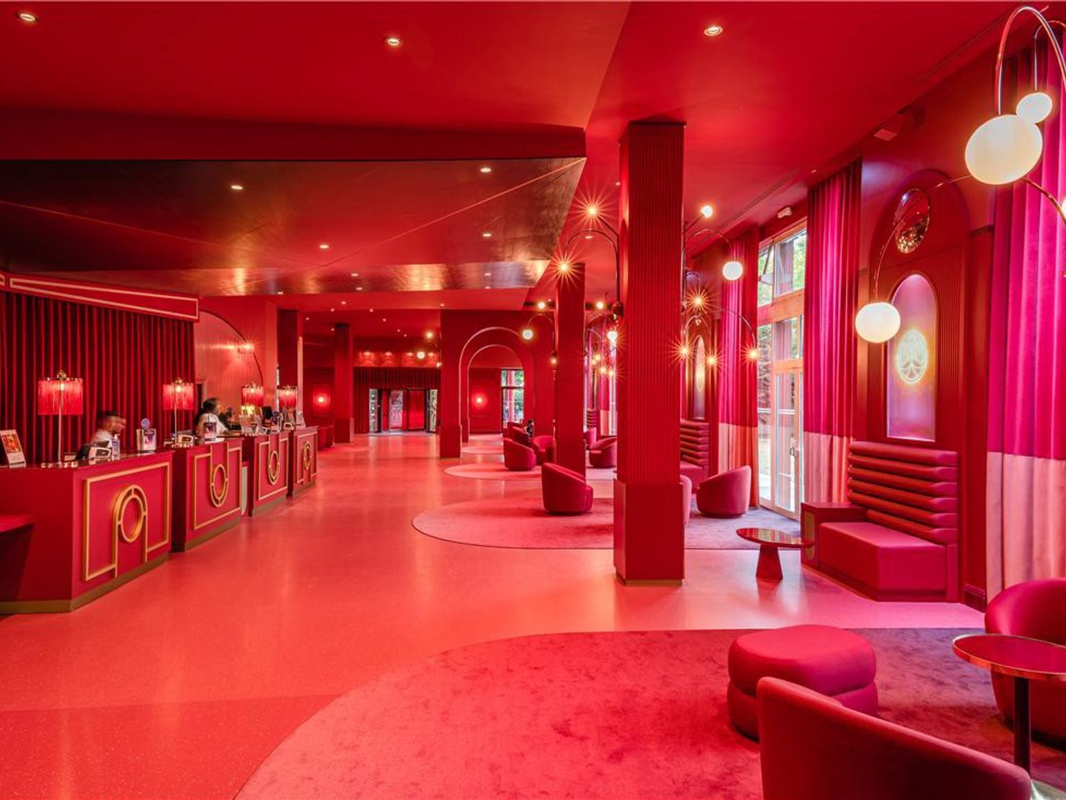 En overdådig hotellobby designet i en monokromatisk rød palett, med resepsjonsdisker, myke sitteplasser og dramatisk belysning. Grand Magic Hotel