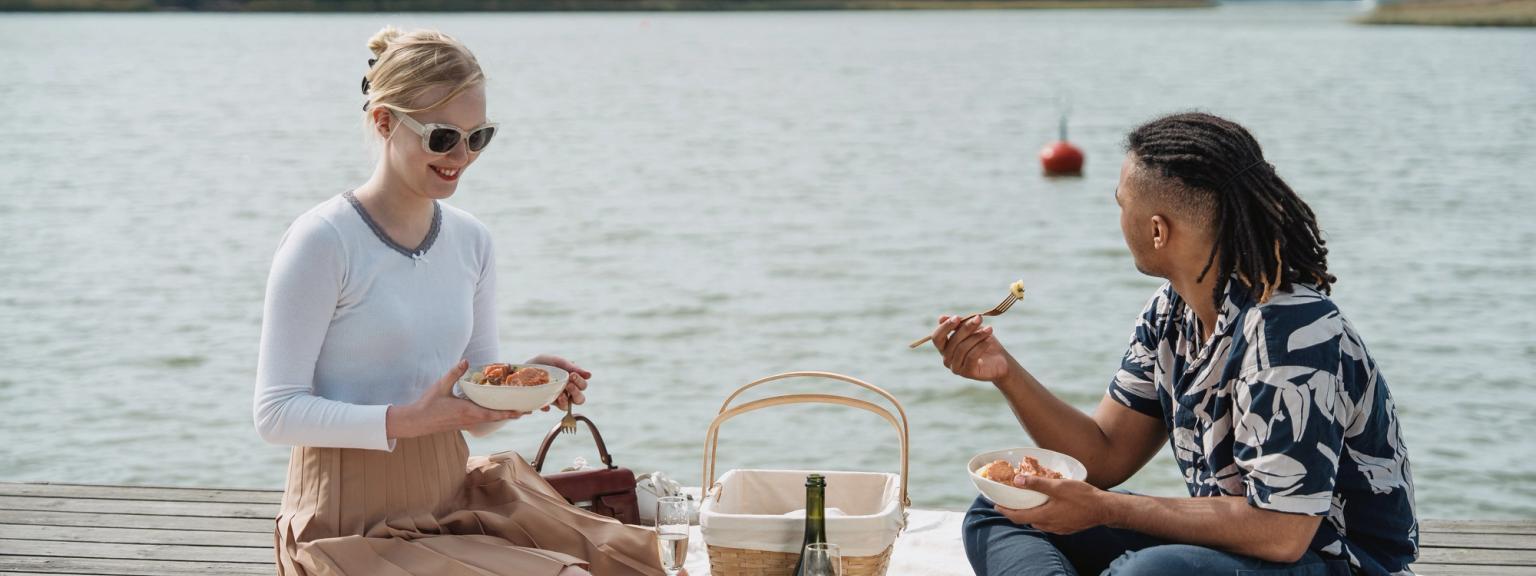 To personer nyder en picnic på en bro ved vandet.