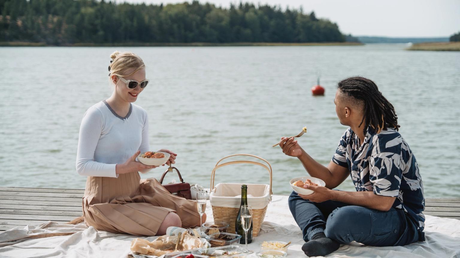 To personer nyder en picnic på en bro ved vandet.