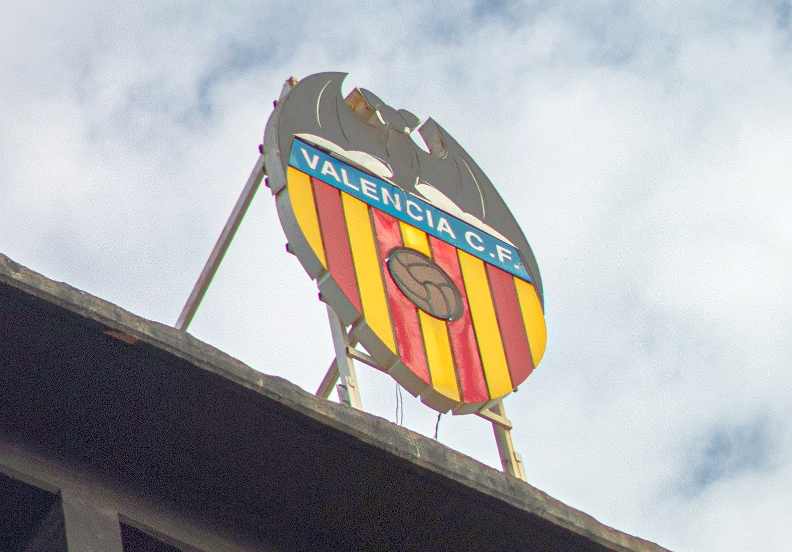 Valencia C.F. logo sign atop a stadium against a cloudy sky.