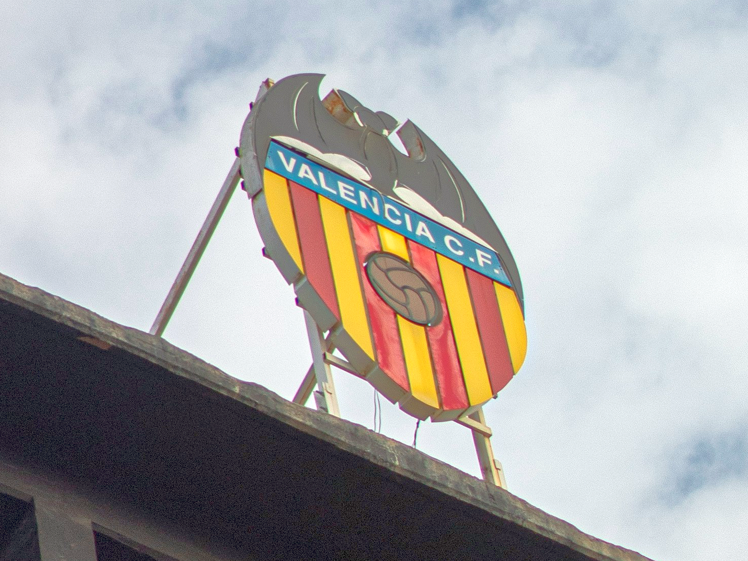 Valencia C.F. logo sign atop a stadium against a cloudy sky.