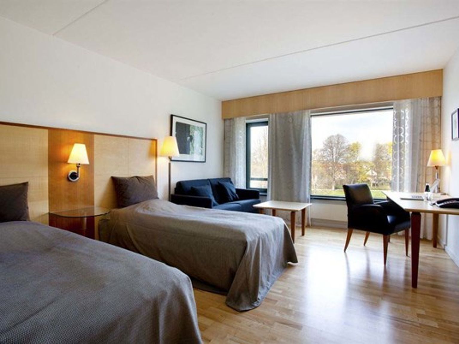 et hotellrom med to senger, en sofa, et skrivebord og et stort vindu