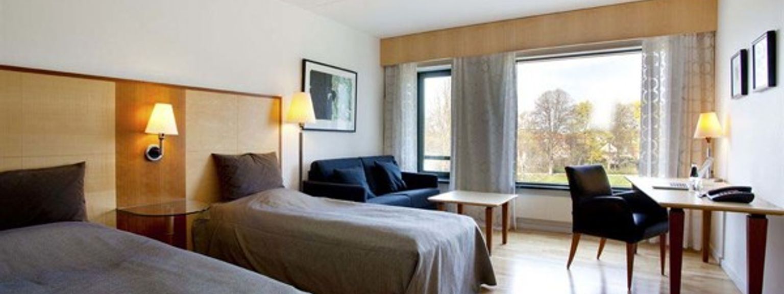 ett hotellrum med två sängar, en soffa, ett skrivbord och ett stort fönster