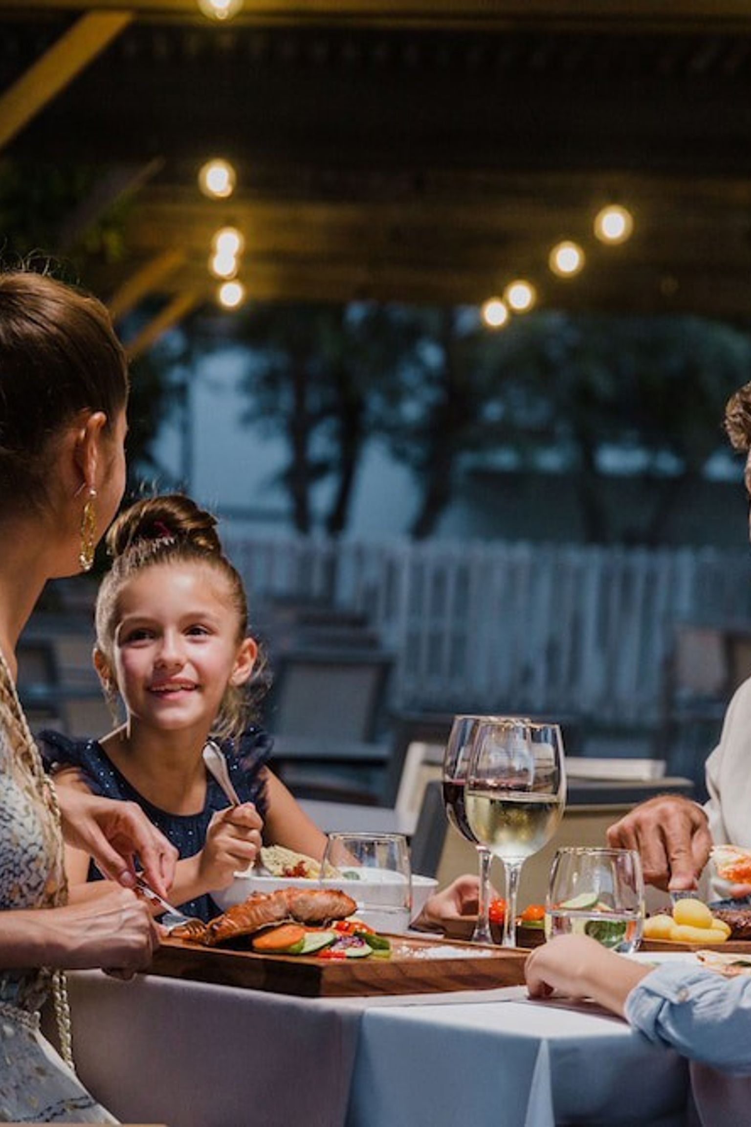 A family of four enjoys an outdoor dinner at night under string lights. Aparthotel Club del Sol Resort & SPA