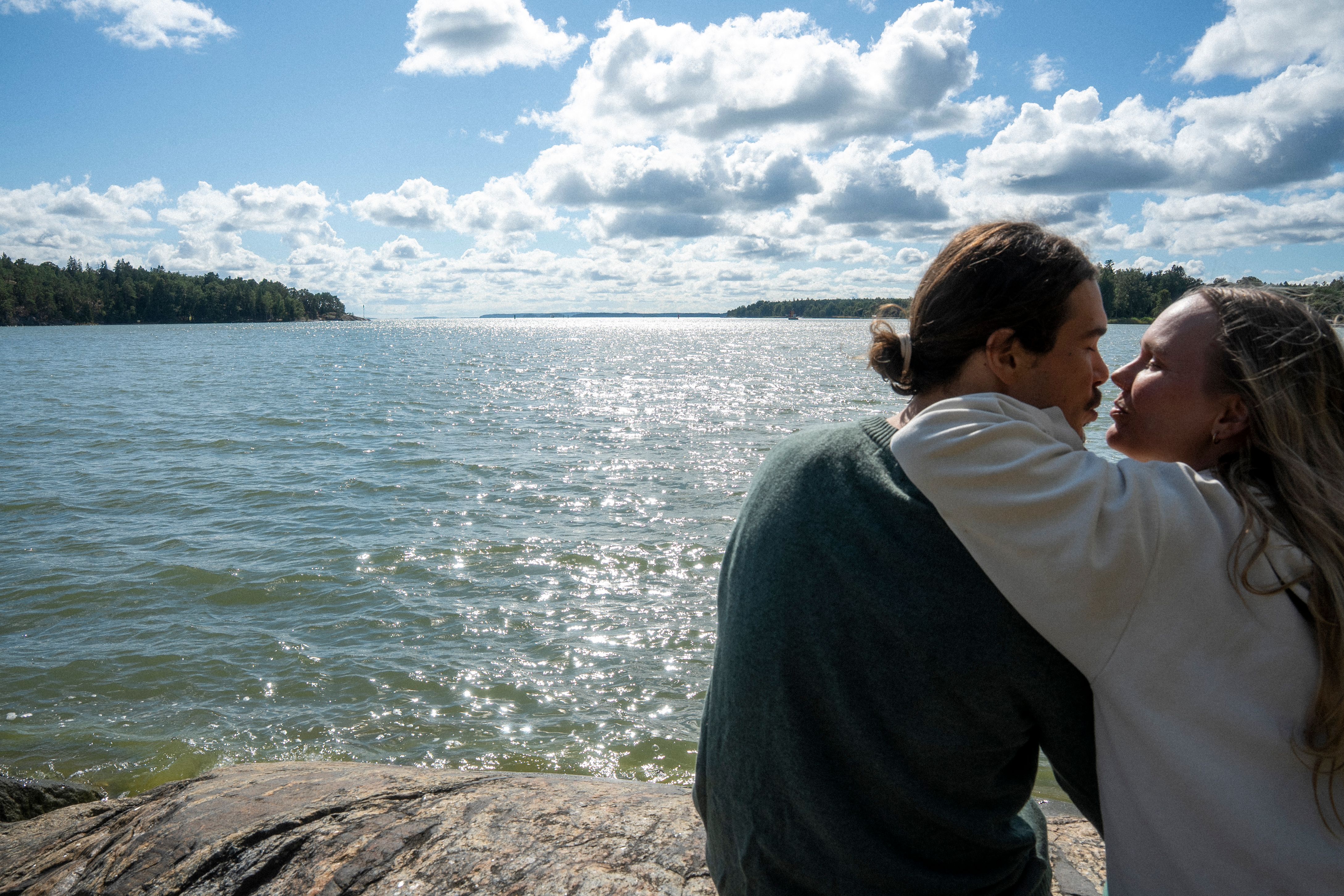 Et par læner sig ind for at kysse ved det funklende vand under en delvist overskyet himmel.