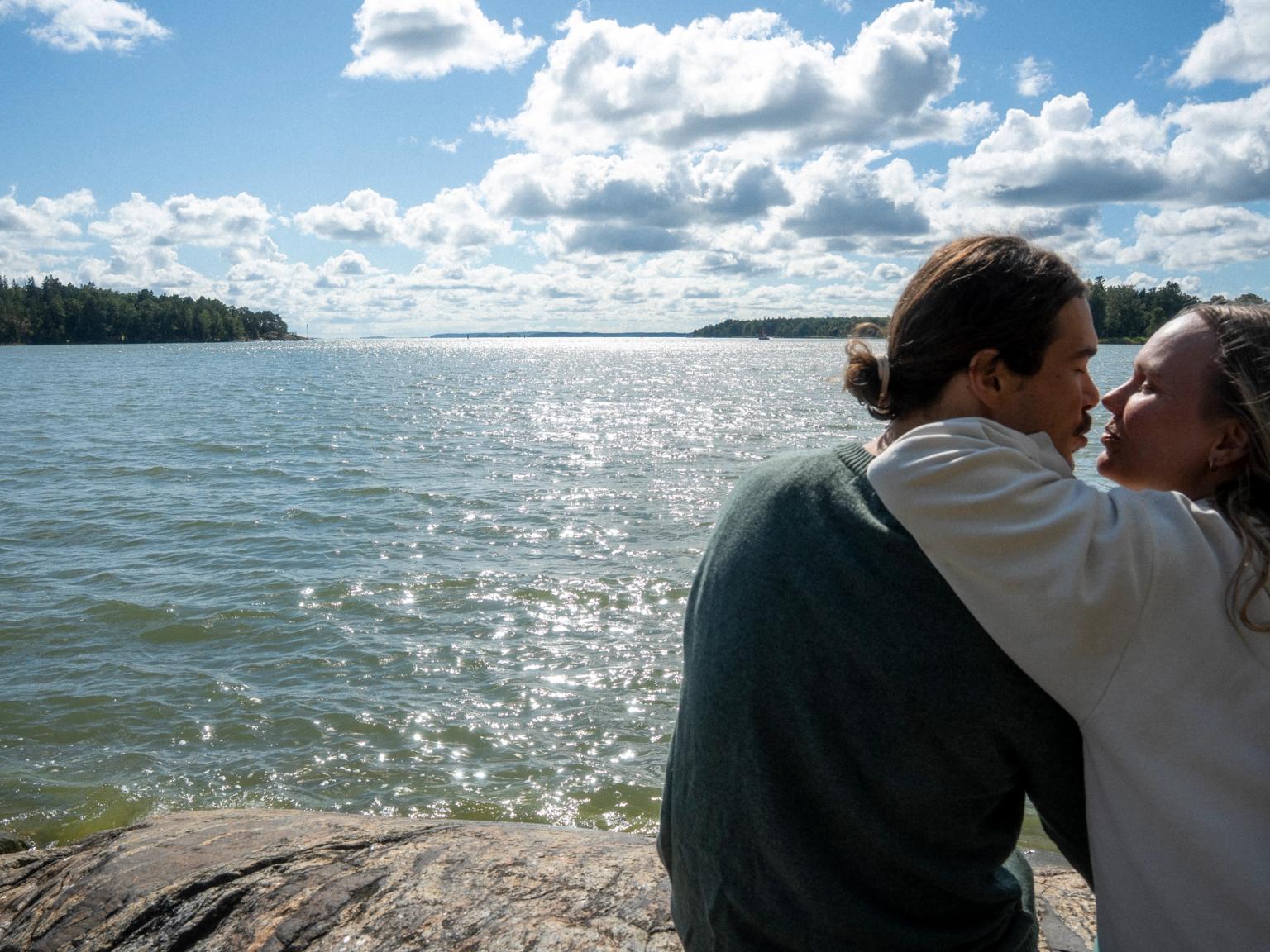 Et par læner sig ind for at kysse ved det funklende vand under en delvist overskyet himmel.