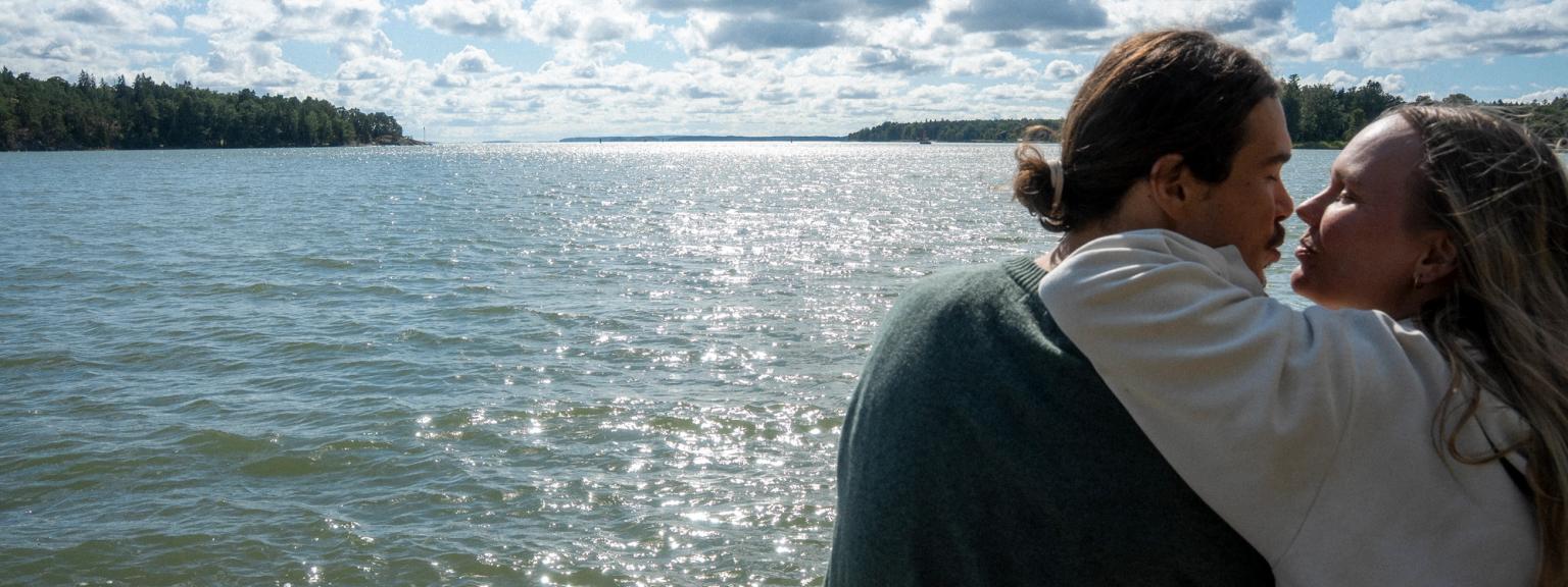 Et par læner sig ind for at kysse ved det funklende vand under en delvist overskyet himmel.