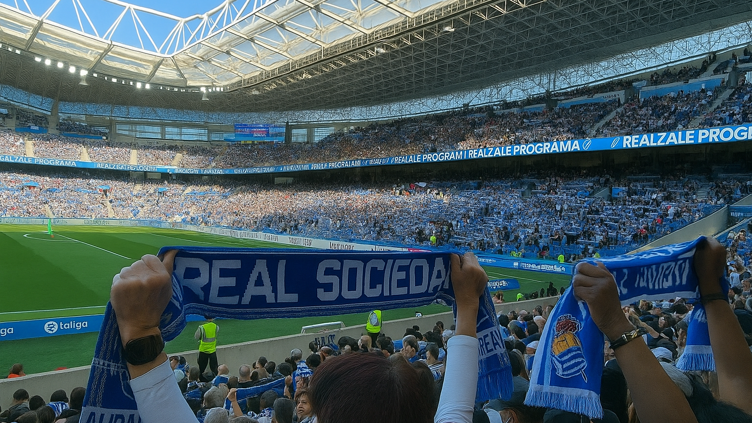 Crowded football stadium with fans holding up Real Sociedad scarves.