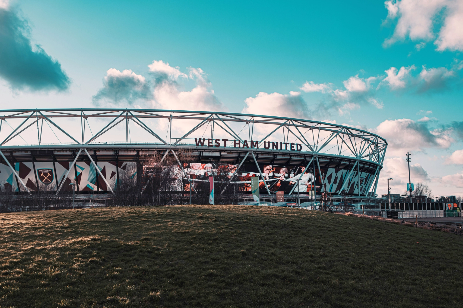 Exterior of West Ham United stadium with a grassy hill and blue sky.