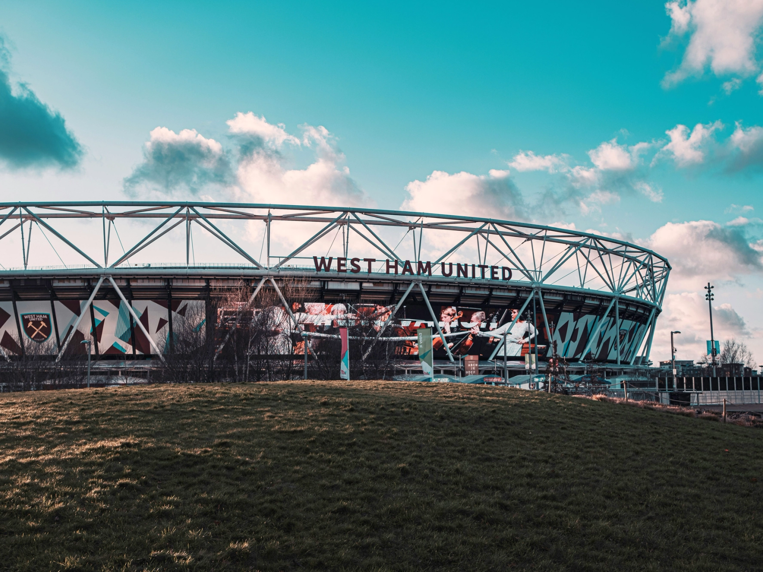 Udvendig af West Ham United stadion med en græsbakke og blå himmel.
