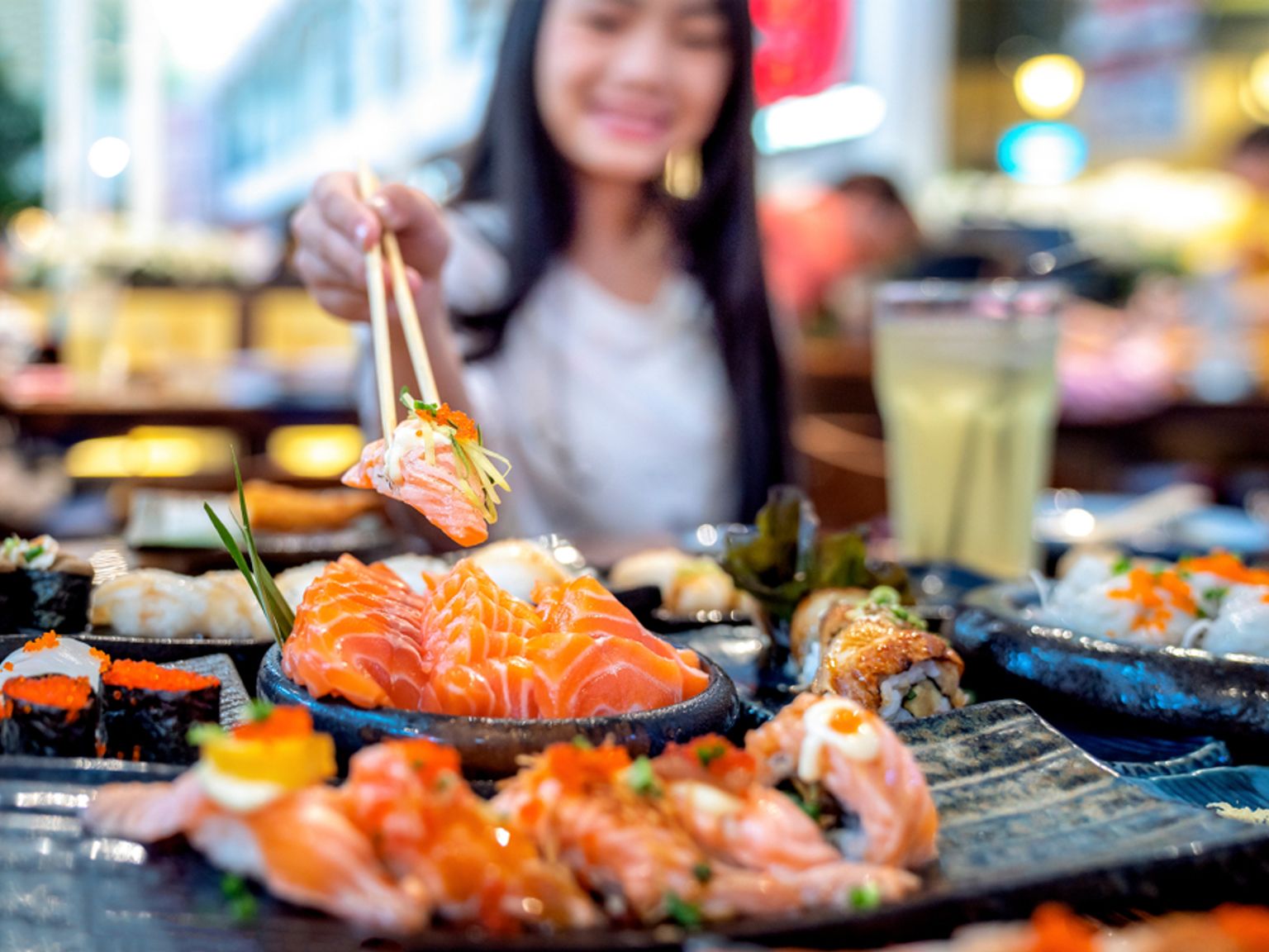 En person tager et stykke laksesushi med spisepinde fra et bord fyldt med forskellige sushiretter. Tokyo, Japan