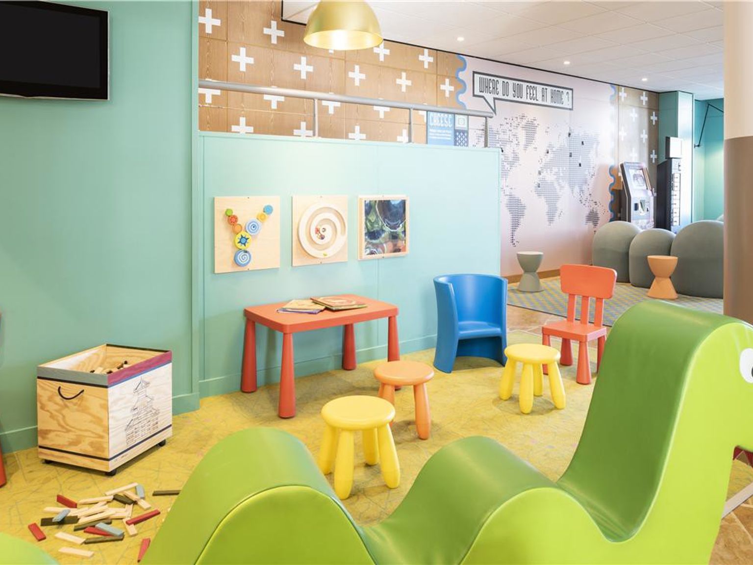 Et fargerikt lekeområde for barn med små bord og stoler, en grønn dinosaurformet myk lekestruktur og leker på gulvet. Adagio Aparthotel Val d'Europe nær Disneyland® Paris