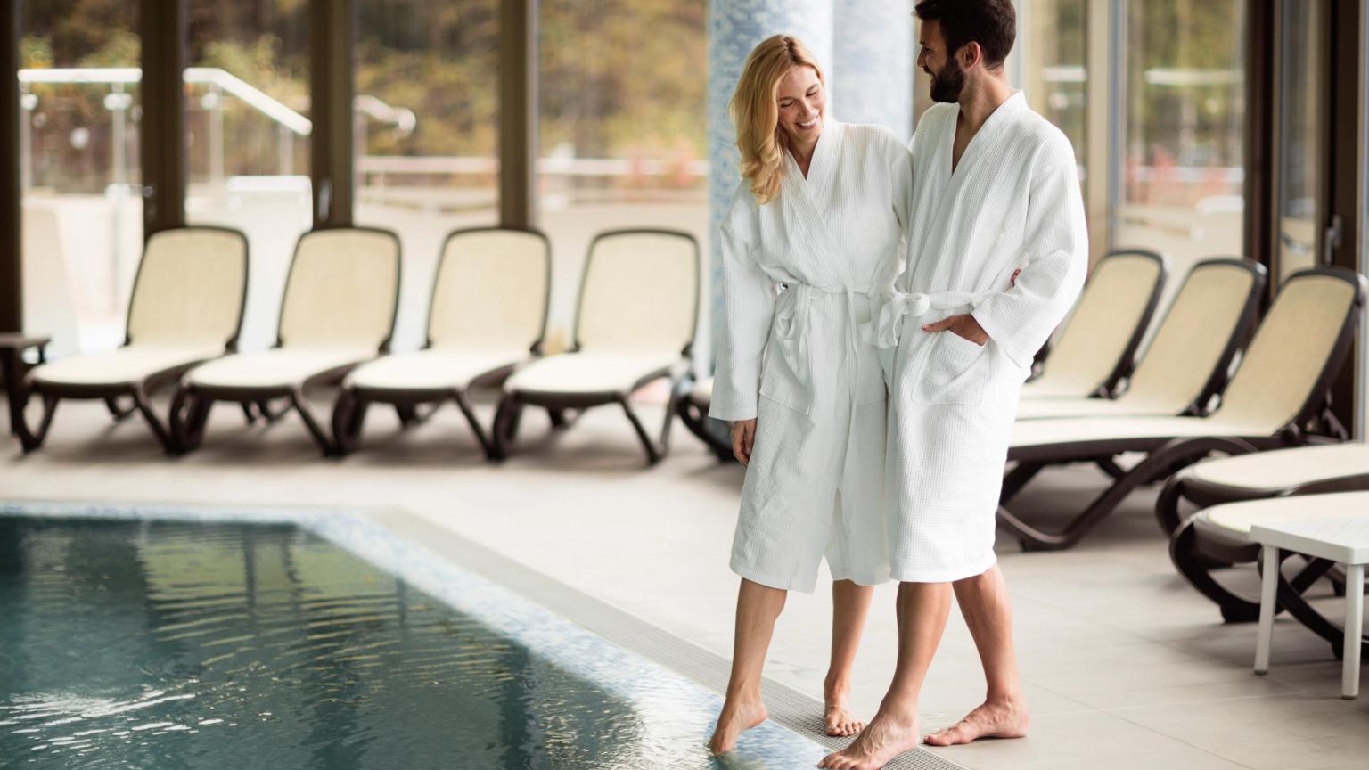 en man och en kvinna i badrockar står bredvid en simbassäng