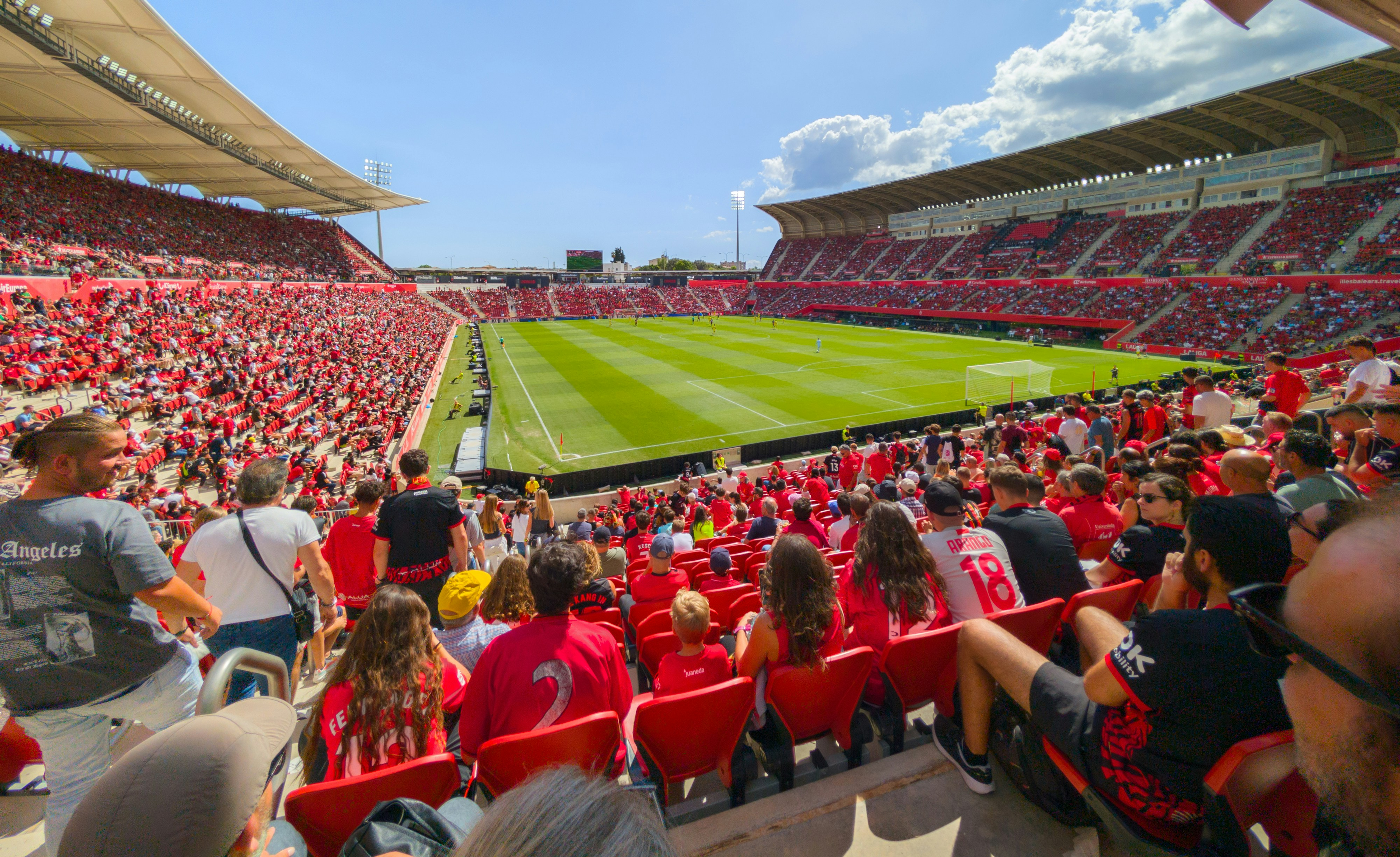 En stor stadion full med människor i rött som tittar på en fotbollsmatch på en solig dag.