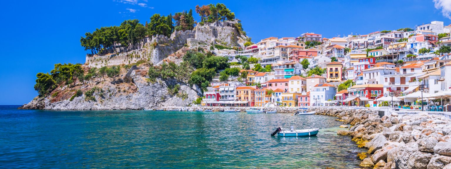 Fargerik kystby i en åsside med et slott og klart blått vann.